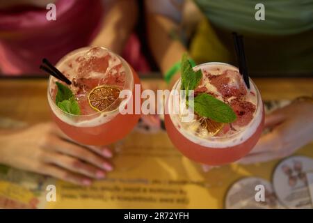 Two young woman drinking fresh pink cocktails with mint, gin and juice in a bar. Two glasses with beverages shot directly from above on a table Stock Photo