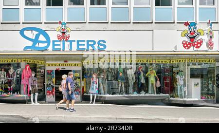 Couple walking past landmark costume shop Deiters in Cologne Germany. Famous for selling outfits for Carnival festival every February. Stock Photo
