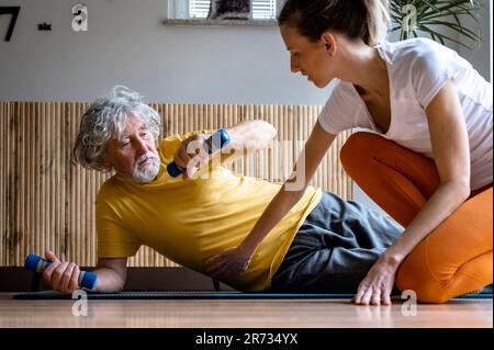 Personal trainer or a physiotherapist working with an elderly man teaching him how to work out properly with dumbbells to stay fit and healthy. Stock Photo