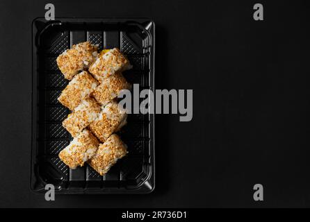 Sushi rolls with salmon, mango, cream cheese, sprinkled with sesame seeds in a package on a black background, top view. Stock Photo