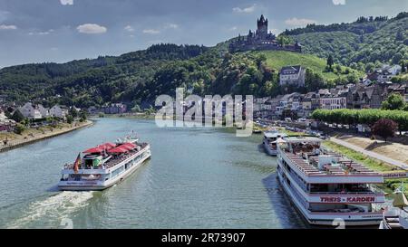 Colorful umbrellas on Moselle River cruise ship as it glides past Medieval town of Cochem, Germany.  Castle in the distance.  Boat moored along banks. Stock Photo