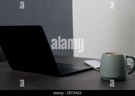 close up of workspace with a black laptop, blank notebook and green cup of coffee Stock Photo