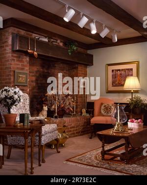 Traditional living room interior with exposed wood beams, brick fireplace, upholstered chairs, warm lighting, and classic home décor accents. Stock Photo