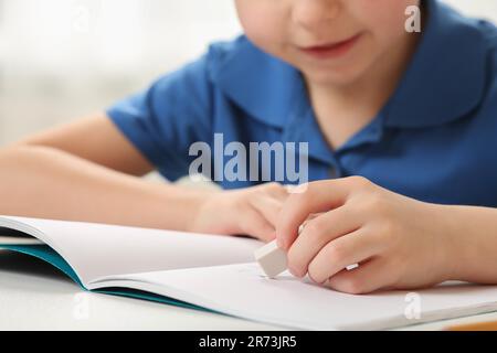 Little boy erasing mistake in his notebook at white desk, closeup Stock Photo