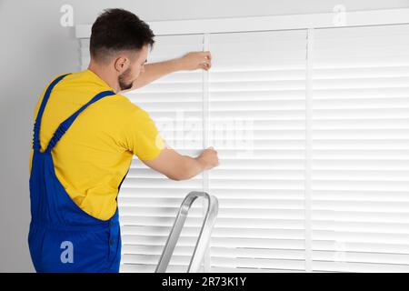 Worker in uniform installing horizontal window blinds indoors Stock Photo