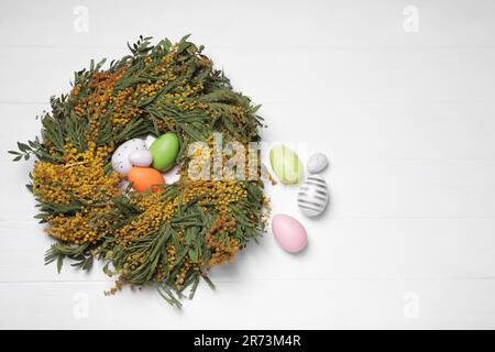 Festively decorated Easter eggs and nest of beautiful spring flowers on white wooden table, flat lay. Space for text Stock Photo