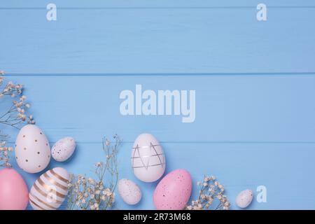 Flat lay composition with festively decorated Easter eggs and gypsophila flowers on light blue wooden table. Space for text Stock Photo