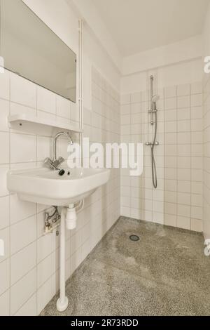 a bathroom with a sink, mirror and shower head mounted on the wall next to it is an empty white tiled floor Stock Photo