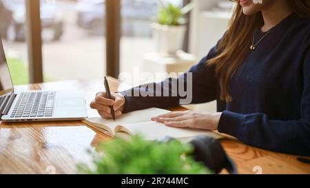 Close-up image of a beautiful woman in casual clothes writing something on her book, writing her diary, making notes, or doing homework. Stock Photo