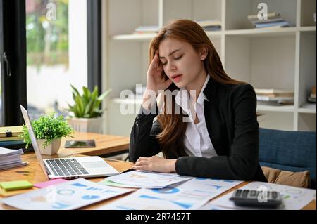 Stressed and upset Asian businesswoman or female financial manager working on financial reports at her desk, feeling overworked and tired of the probl Stock Photo