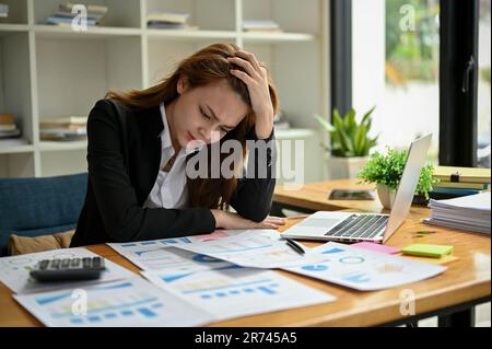 A stressed and frustrated Asian businesswoman is working on a business financial reports and, feeling tired and overworked, can't figure out the probl Stock Photo
