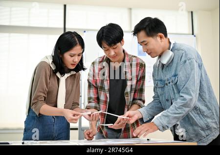 A team of professional Asian graphic designers or tech developers is sharing ideas, brainstorming and discussing their new project in the meeting room Stock Photo