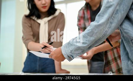 A close-up image of a team of professional tech startup or app developers discussing work and reviewing a new app prototype in the meeting together. Stock Photo