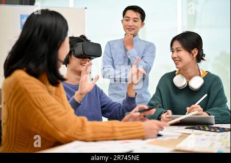 An excited young Asian male developer tested a new virtual reality headset with his team in the creative office. technology, innovation, tech startup Stock Photo