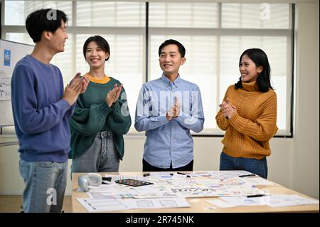 A group of cheerful Asian graphic designers or developers is standing in the meeting, clapping their hands, and celebrating their successful project i Stock Photo