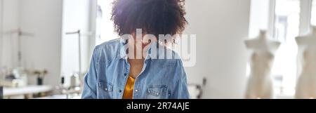 Professional African-American dressmaker draws pattern on fabric working at cutting table Stock Photo
