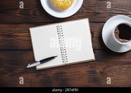 Cup of coffee, donut and opened notebook on wooden table, top view Stock Photo