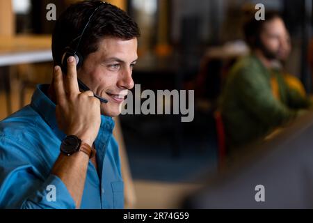 Smiling caucasian casual businessman using phone headset and using computer in casual office Stock Photo