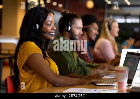 Happy diverse colleagues in phone headsets using computers in office Stock Photo