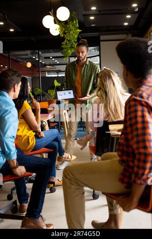 Caucasian casual businessman presenting to diverse colleagues using tablet in office Stock Photo