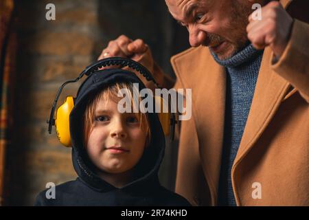 The father yells at the child. Young boy wearing headphones from noise. Home conflict, parenting problems concept. Stock Photo