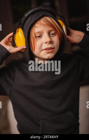 A young boy in big headphones against noise on a dark background. Stock Photo