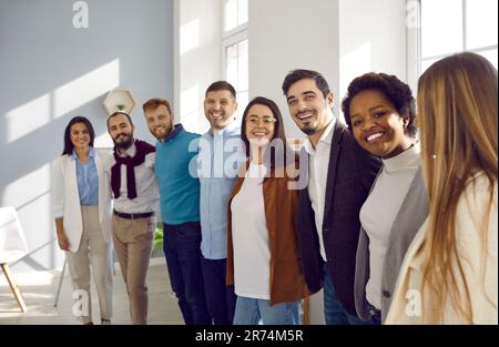 Multiethnic team of happy supportive business people standing in office, hugging and smiling Stock Photo