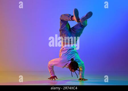 Flexible young man, contemp dancer performing breakdance, hip-hop against gradient multicolored studio background in neon light Stock Photo