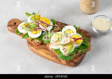 Two homemade sandwiches with egg, arugula and cheese sprinkled with sesame seeds on wooden board Stock Photo