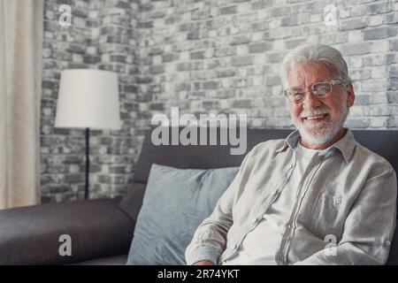 Portrait of happy mature 80s man sit on couch at home look at camera posing relaxing on weekend, smiling positive senior 70s grandfather rest on sofa at home or retirement house, show optimism Stock Photo