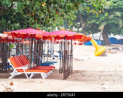 Beach in Pattaya, Thailand with empty beach chairs and a yellow buoy in the background stranded on the beach. Trees over the parasols and in the backg Stock Photo