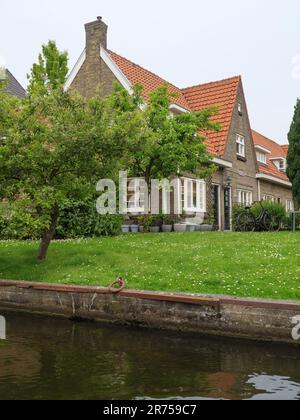 A traditional coastal house with red-tiled roofs and a small wooden boat docked next to it, situated on a tranquil beach overlooking the ocean Stock Photo