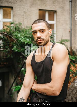 man, short hair, three day beard, shirt on arm, black, courtyard, half portrait Stock Photo