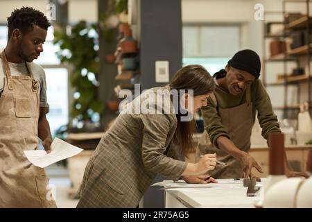Ceramics studio owner and two workers discussing designs Stock Photo