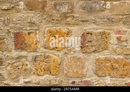 the stone wall is made of colored, large stones, tightly stacked on top of each other with cement mortar, the surface of the wall is uneven and rough. Stock Photo