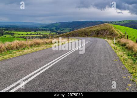 Plain asphalt road turning right through Adelaide Hills farms during winter season, South Australia Stock Photo