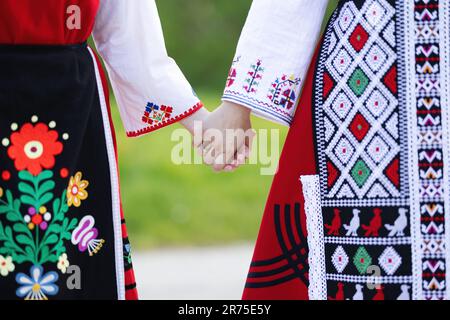 Girls in traditional bulgarian ethnic costumes with folklore embroidery holding hands. The spirit of Bulgaria - culture, history and traditions. Stock Photo