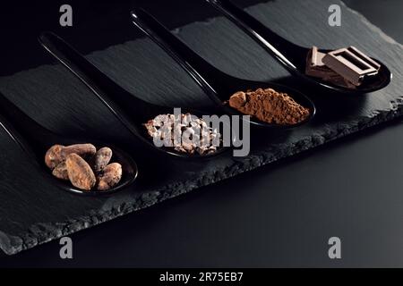 Chocolate bar, cocoa powder, cacao beans and nibs, heap in wooden spoons, chocolate background Stock Photo