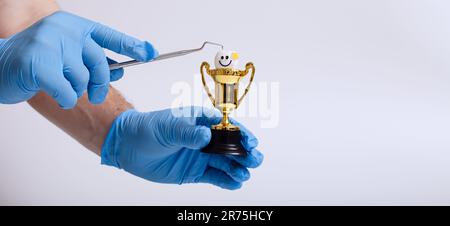 A man in a blue medical glove holds a gold trophy on a white background. Stock Photo