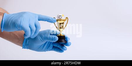 A man in a blue medical glove holds a gold trophy on a white background. Stock Photo