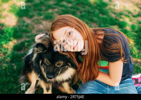 Outdoor portrait of cute red-hired kid girl hugging her dog Finnish Lapphund Stock Photo