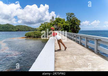 North America, Caribbean, Greater Antilles, Hispaniola Island, Dominican Republic, Sama Province, Sama Peninsula, Santa rbara de Sama, Pretty Latina leans on the railing of the iconic bridge and looks over the bay of Sama Stock Photo