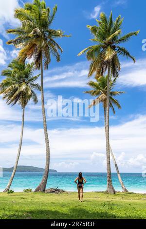 North America, Caribbean, Greater Antilles, Hispaniola Island, Dominican Republic, Sama Province, Sama Peninsula, Las Galeras, Playa Colorada, Pretty Latina standing between palm trees on Playa Colorada Beach Stock Photo