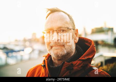 Outdoor portrait of middle age man wearing eyeglasses and orange winter jacket Stock Photo