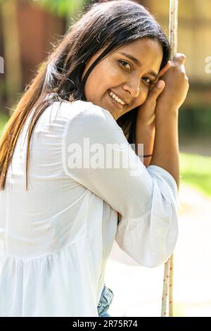 North America, Caribbean, Greater Antilles, Hispaniola Island, Dominican Republic, North Coast, Puerto Plata Province, Cabarete, Young woman sitting on swing and holding on to rope Stock Photo