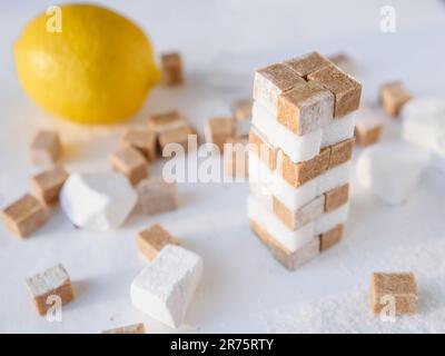 A tower of white and brown sugar cubes and fresh lemon in the background. Sweet and sour food concept. Stock Photo