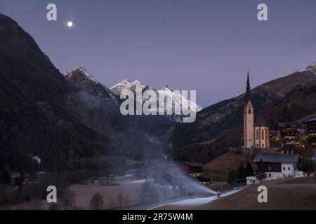Parish church St.Vinzenz, Heiligenblut am Großglockner, in the morning at blue hour with running snow cannons and moon Stock Photo