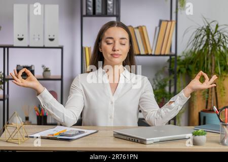 Caucasian business woman working on laptop computer, meditating doing yoga breathing exercise in lotus position at home office. Calm serene freelancer girl taking break. Busy occupation. Peace of mind Stock Photo