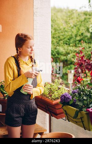 Adorable little girl watering plants on the balcony on a nice sunny day Stock Photo