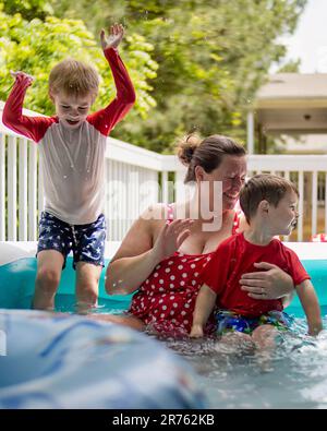 A smiling woman and two happy boys are enjoying their day in a swimming pool. Stock Photo